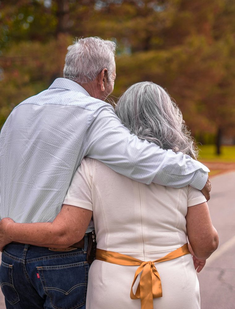 An older couple walking arm in arm down a tree-lined road